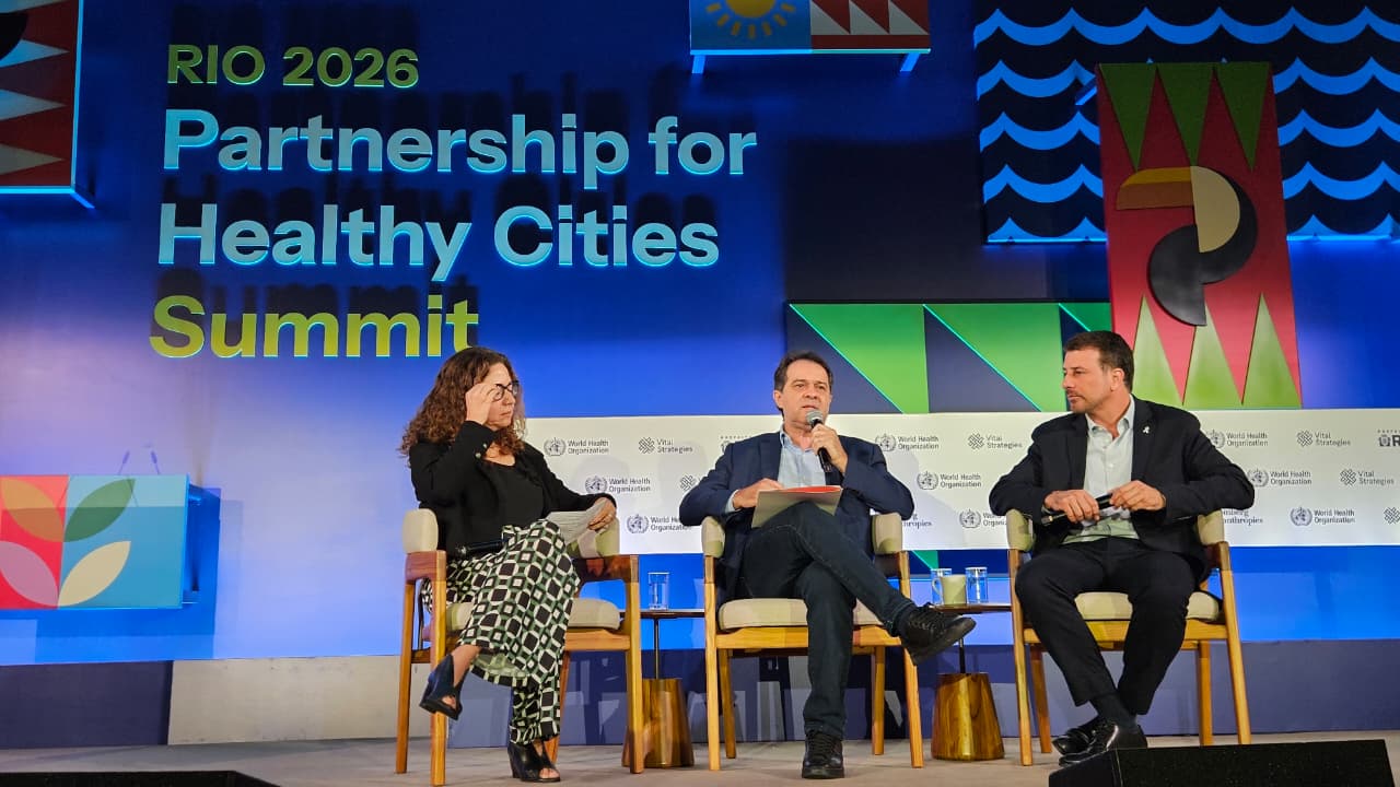 O prefeito Evandro Leitão está sentado em uma cadeira, discursando no palco da 4ª Cúpula da Parceria para Cidades Saudáveis